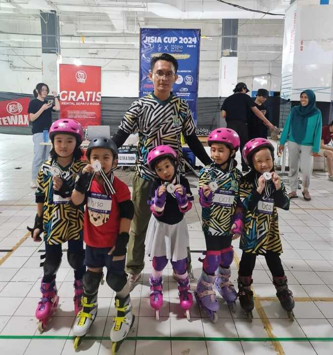 lima orang anak menggunakan medali dan menggunakan sepatu roda di dampingi oleh seorang pelatih