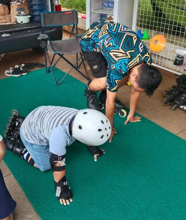 gambar seorang anak yang belajar inline skate dengan menggunakan protektor yang lengkap dan di dampingi pelatih