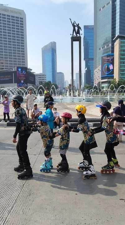 kegiatan lima orang bermain sepatu roda di tengah kota dan terdapat patung